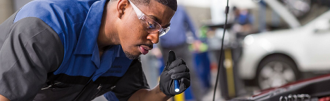 A Subaru technician using flashlight to look into a Subaru engine compartment.