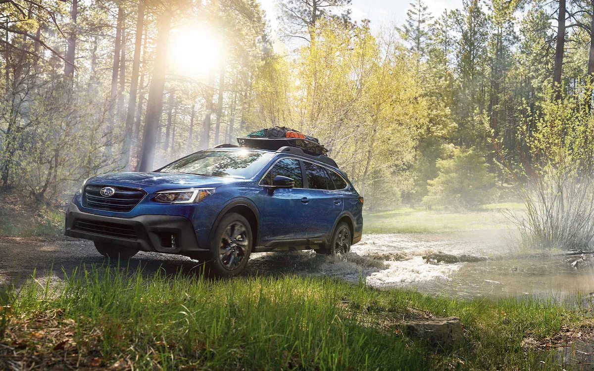 A 2022 Subaru Outback driving on a backcountry road with a cargo carrier on its standard raised roof rails.
