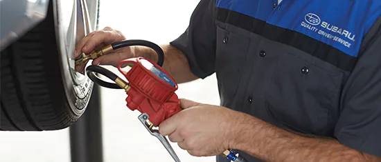 A Subaru service technician checking tire air pressure.